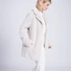 kennedy plush faux fur coat in pearl side Woman wearing the Kennedy plush faux fur coat in pearl, side profile, hands in pockets Back view of the Kennedy plush faux fur coat in pearl showing the wing collar Woman wearing the Kennedy plush faux fur coat in pearl over white trousers, front view